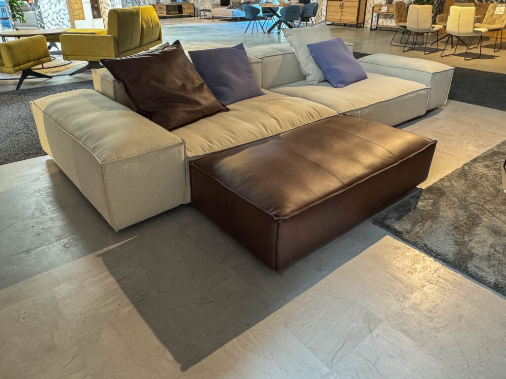 Luxuri&ouml;se Wohnlandschaft mit gro&szlig;en Kissen, Lederhocker und moderner Optik bei M&ouml;bel L&uuml;ckoff in Eschenburg.